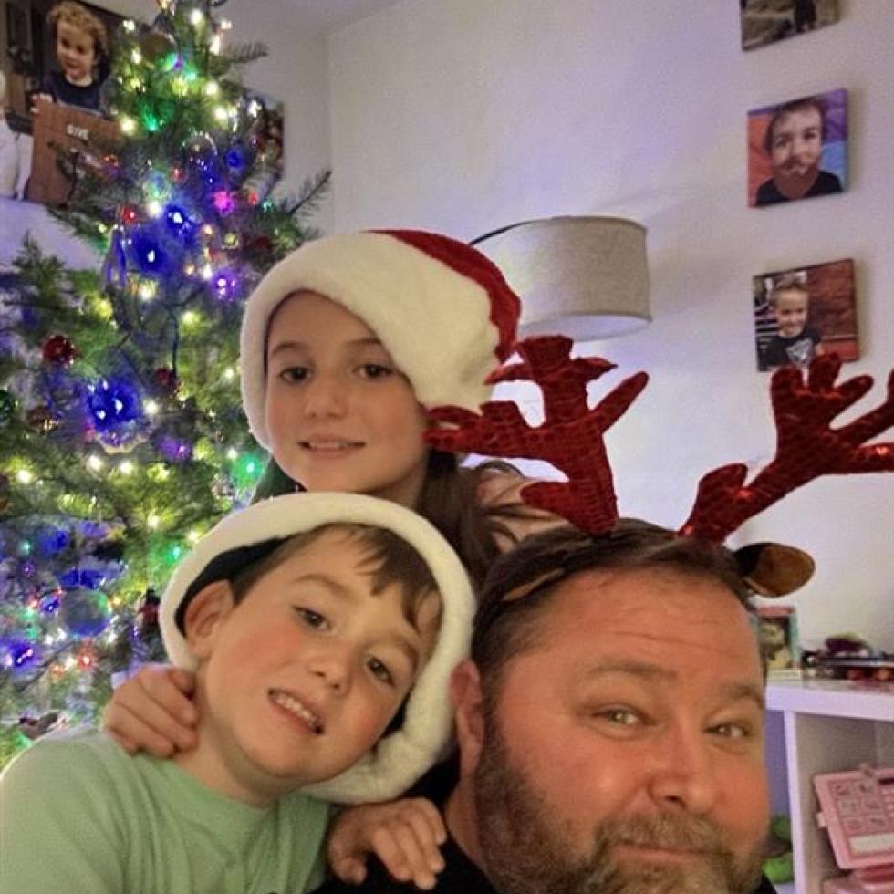 Jeff Davis with his two children, Zoe and Austin. Jeff Davis with his two children: Zoe (9) and Austin (7) wearing red Christmas hats next to a decorated Christmas Tree