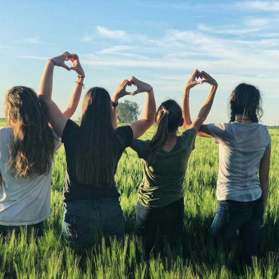 Four girls with their backs turned to the camera making hearts with their hands