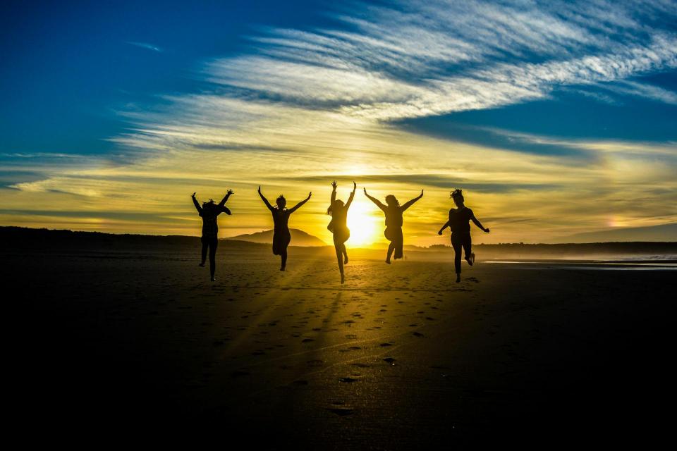 humans leaping in the air with their arms in the air, almost as leaping for joy, with a sunset behind them