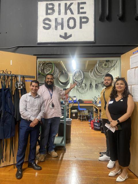 four adults standing in front of a school bike shop with a bike shop sign.