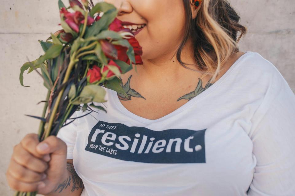 Photot of woman smelling roses wearing a shirt that says "resilient"